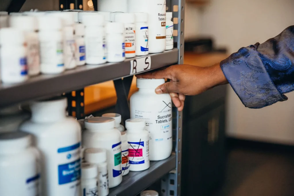 someone grabbing medication from shelf containing many bottles of medications
